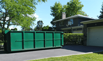 Large green dumpster bin delivered in a residential driveway